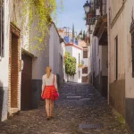 Una joven turista rubia explora las estrechas callejuelas empedradas del casco antiguo (Albaicín o Barrio Árabe) de Granada, Andalucía, España.