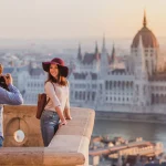 Una giovane coppia si fotografa sul punto panoramico del Bastione dei Pescatori a Budapest all'alba.